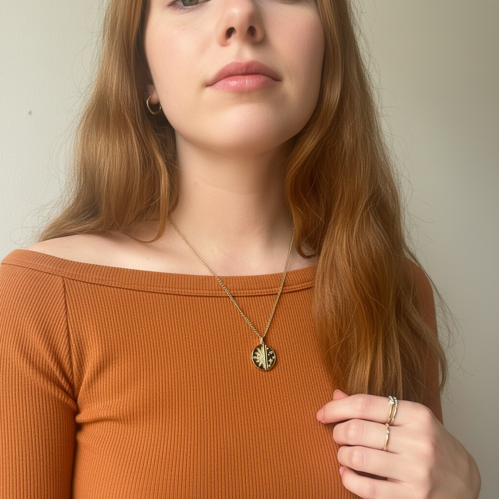 Woman wearing a gold necklace with a pendant against a neutral background