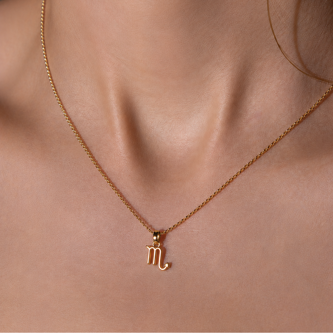 Gold necklace with a Scorpio symbol pendant on a person's neck