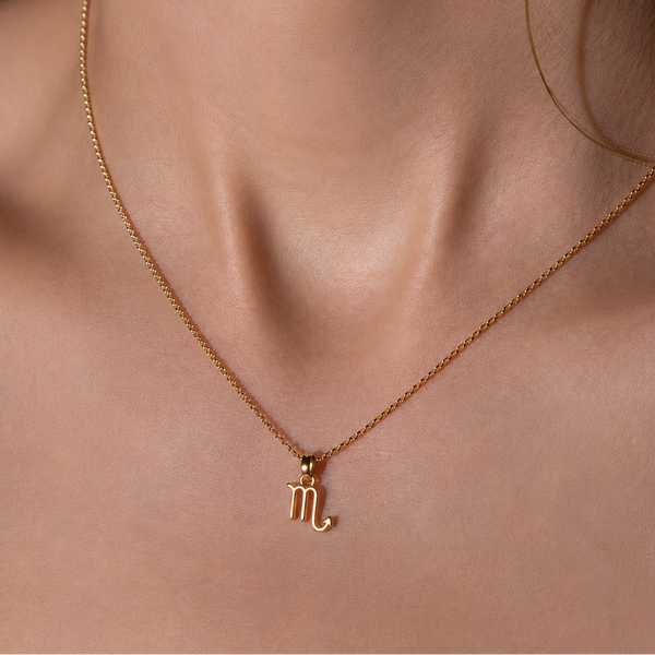 Gold necklace with a Scorpio symbol pendant on a person's neck