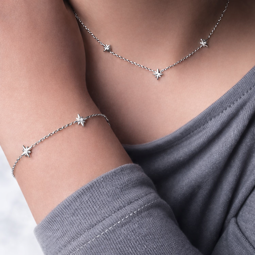 Silver star necklace person's neck and wrist against a neutral background