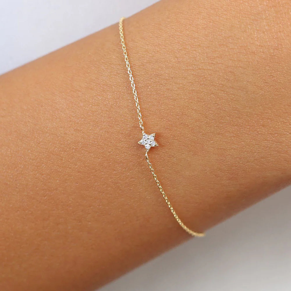 Gold bracelet with a star-shaped charm on a wrist against a light background