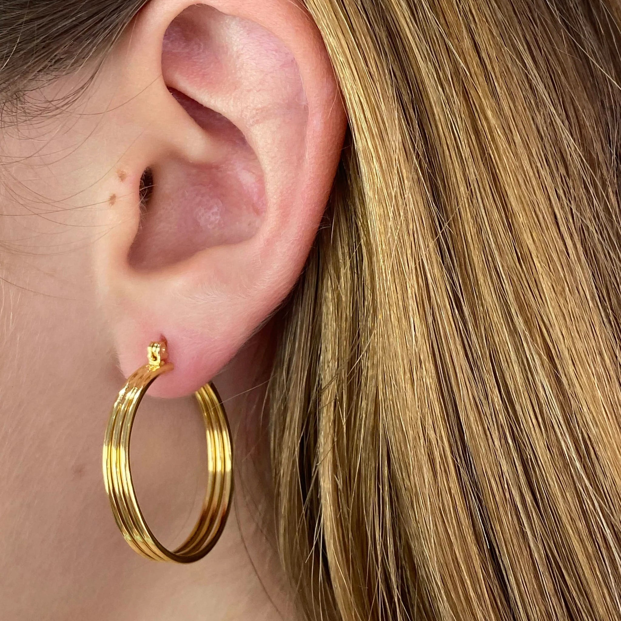 Close-up of an ear wearing a gold hoop earring with blonde hair.