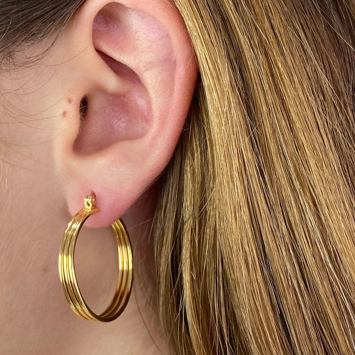 Close-up of an ear wearing a gold hoop earring with blonde hair.