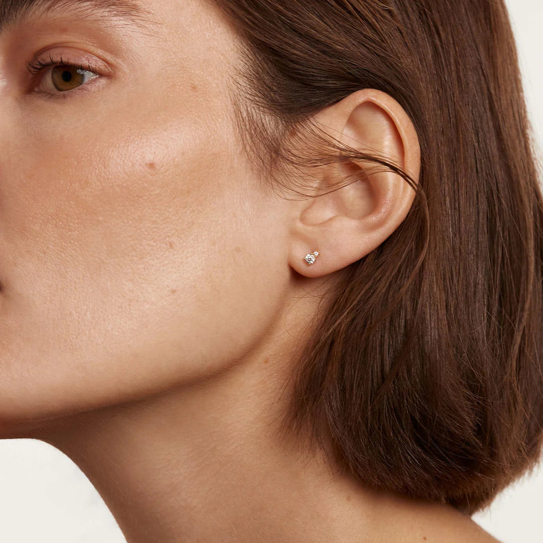 Close-up of a person wearing a small earring on a neutral background