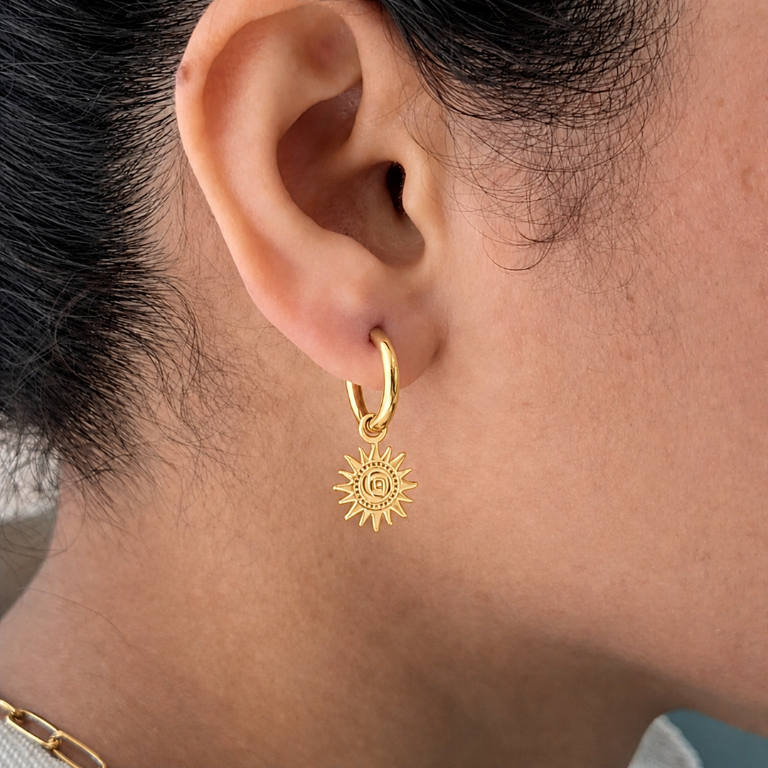 Gold hoop earring with a sun design worn by a person.