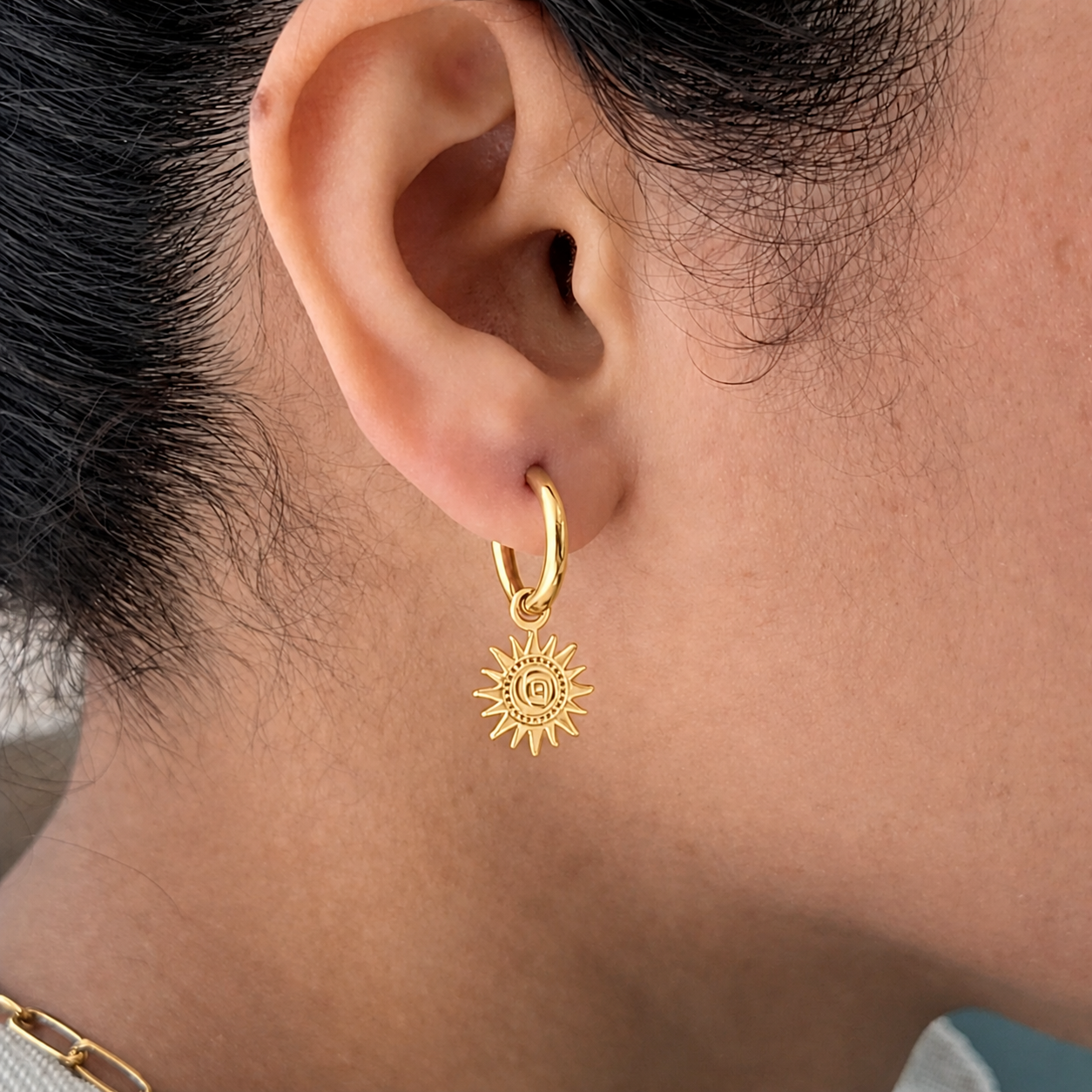 Gold hoop earring with a sun design worn by a person.