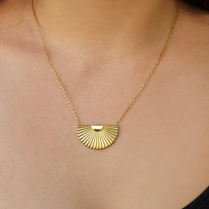Gold necklace with a fan-shaped pendant on a person's neck