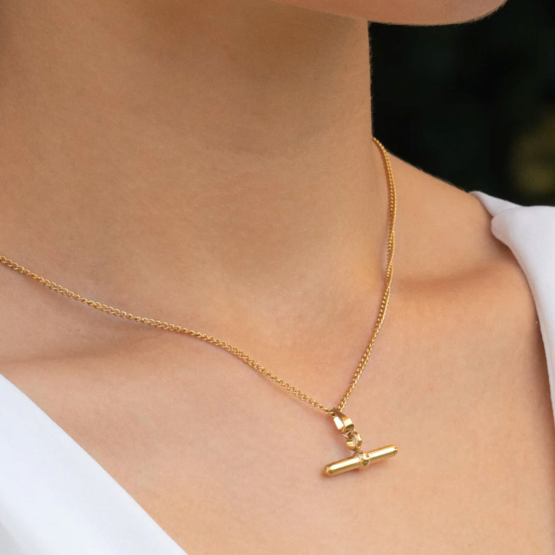 Gold necklace with a pendant on a person wearing a white top.