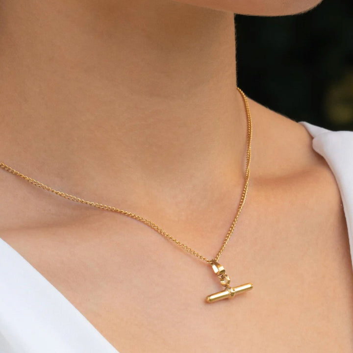 Gold necklace with a pendant on a person wearing a white top.