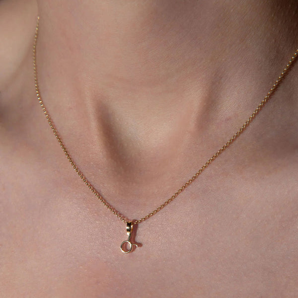 Rose gold necklace with a small pendant on a person's neck against a neutral background
