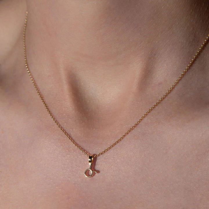 Rose gold necklace with a small pendant on a person's neck against a neutral background