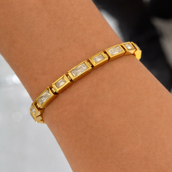 Gold bracelet with diamond accents on a wrist against a neutral background
