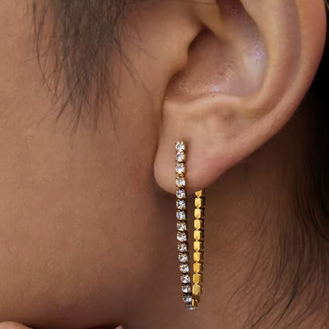 Close-up of an ear wearing gold hoop earrings with clear gemstones.