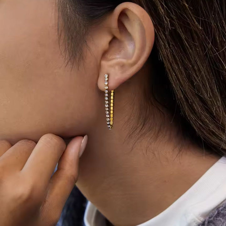Close-up of an ear wearing a gold and diamond earring with a blurred background