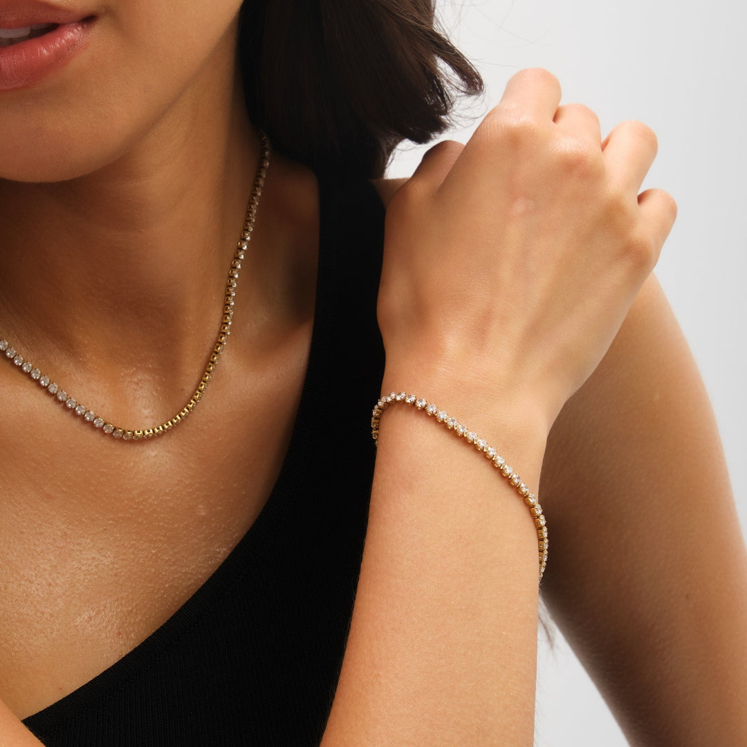 Close-up of a woman wearing a gold necklace and bracelet on a plain background