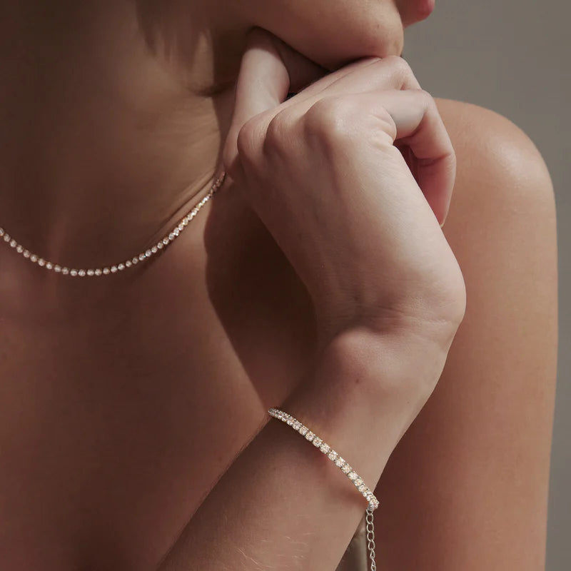 Close-up of a person wearing a delicate silver necklace and bracelet against a neutral background