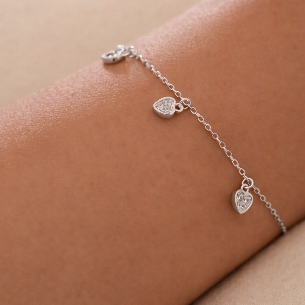 Silver bracelet with heart-shaped charms on a person's wrist against a beige background