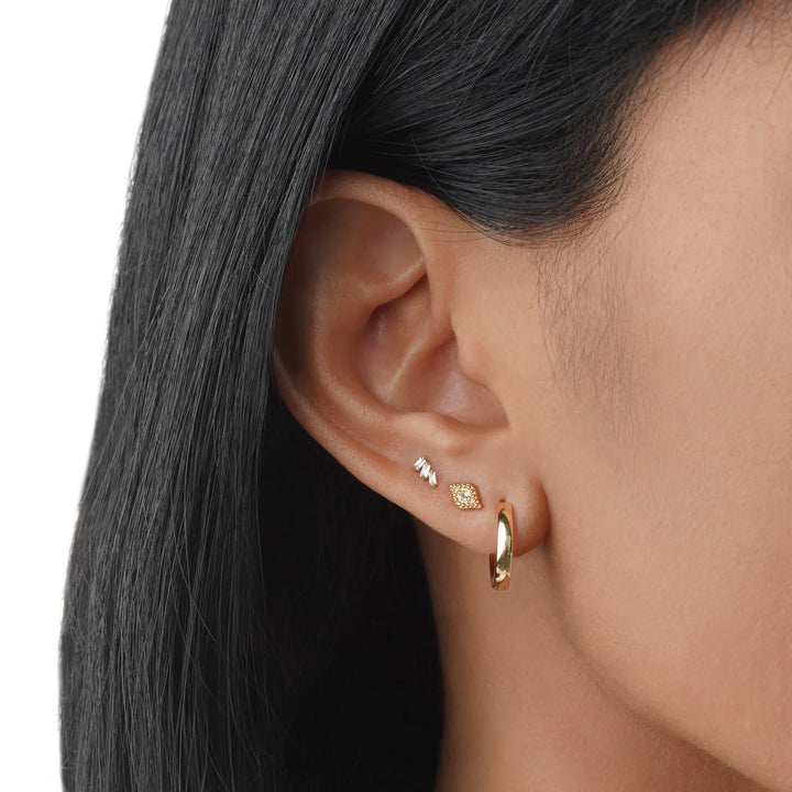 Close-up of an ear wearing gold hoop earrings with a neutral background