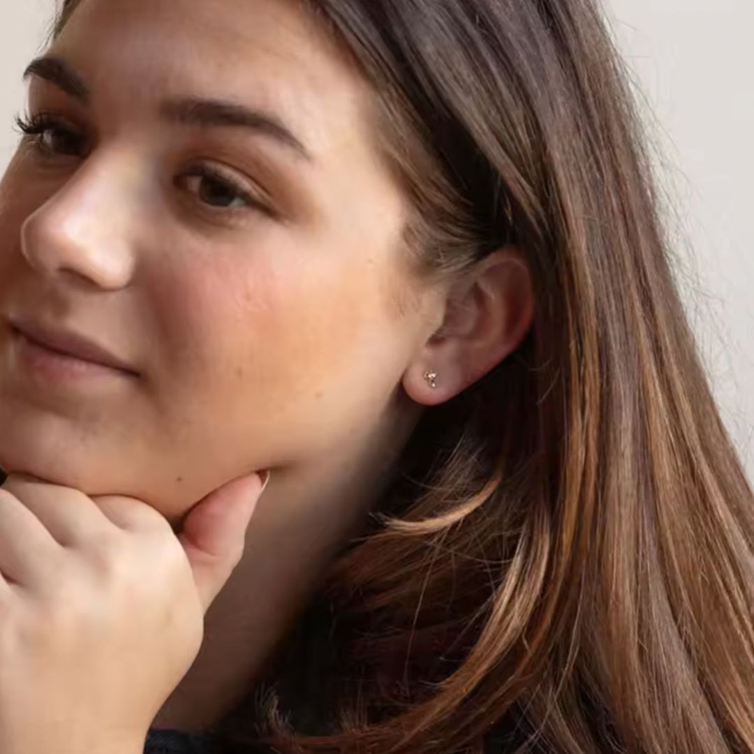 Close-up of a woman with her hand on her chin, wearing a small earring.