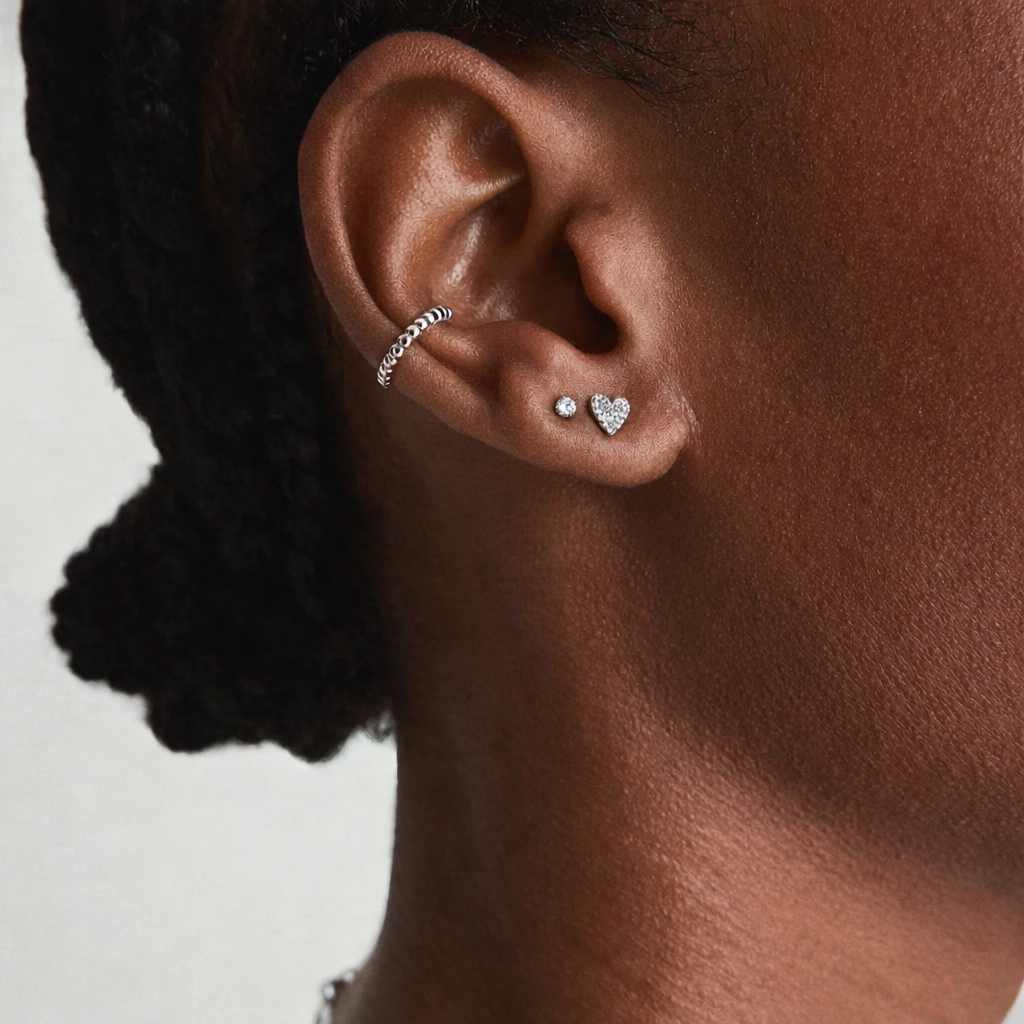 Close-up of an ear wearing a small hoop earring and heart-shaped stud earrings on a neutral background