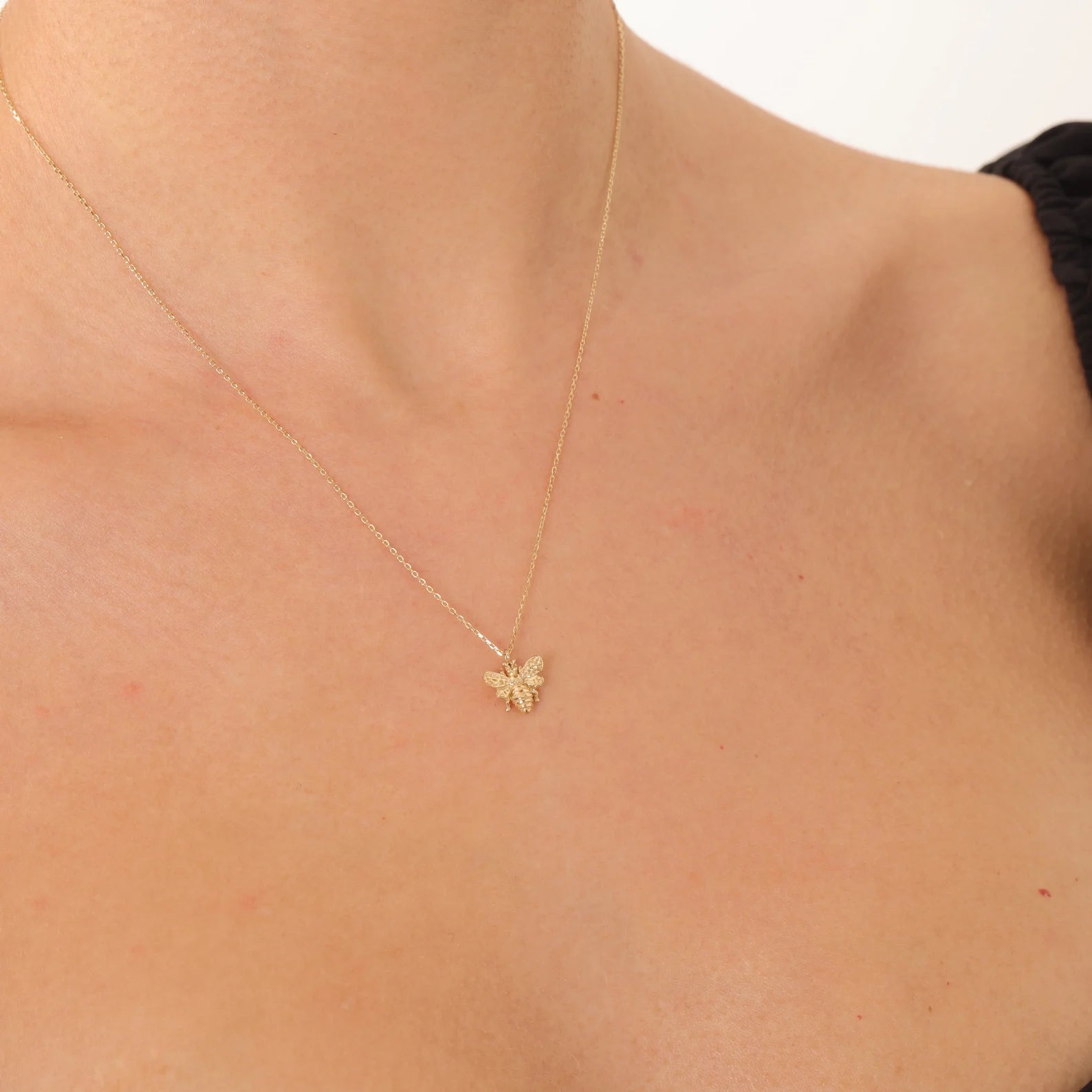 Gold necklace with a butterfly pendant on a person's neck against a white background