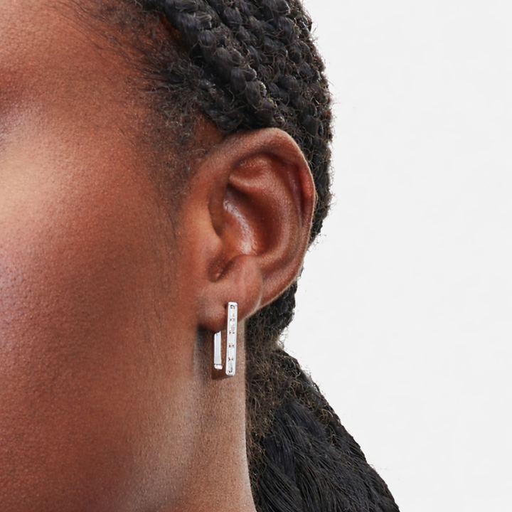 Close-up of an ear wearing a silver earring on a plain background