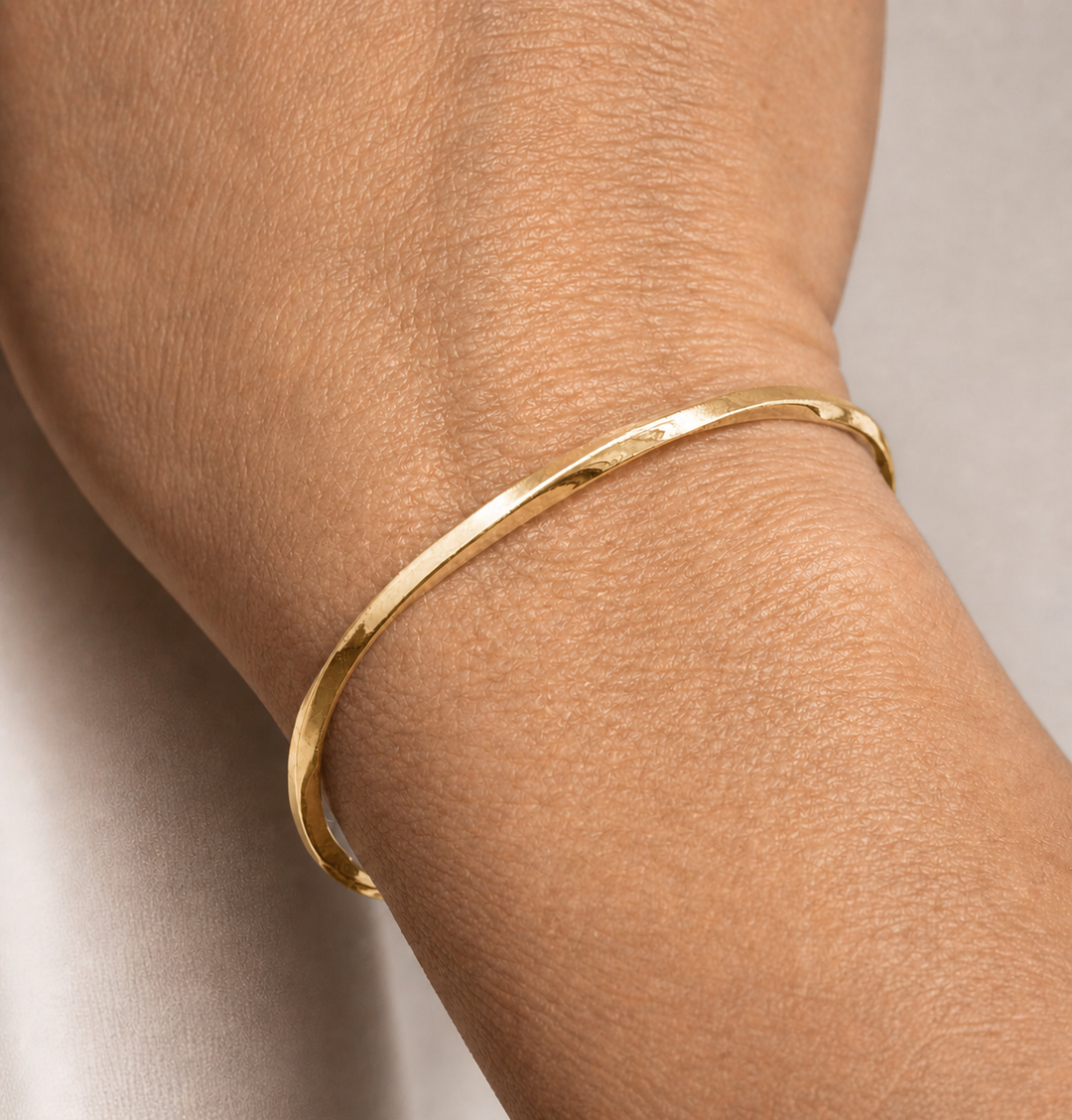 Gold bracelet on a wrist with a neutral background