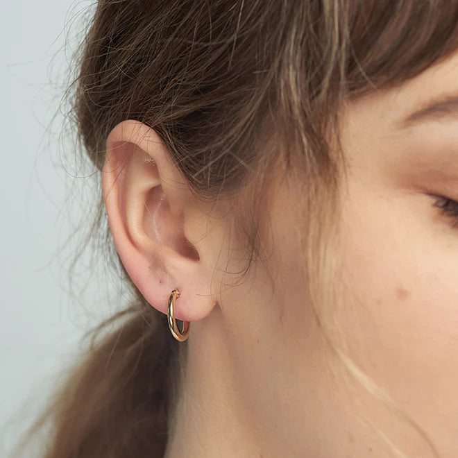 Close-up of a person wearing a gold hoop earring with a neutral background
