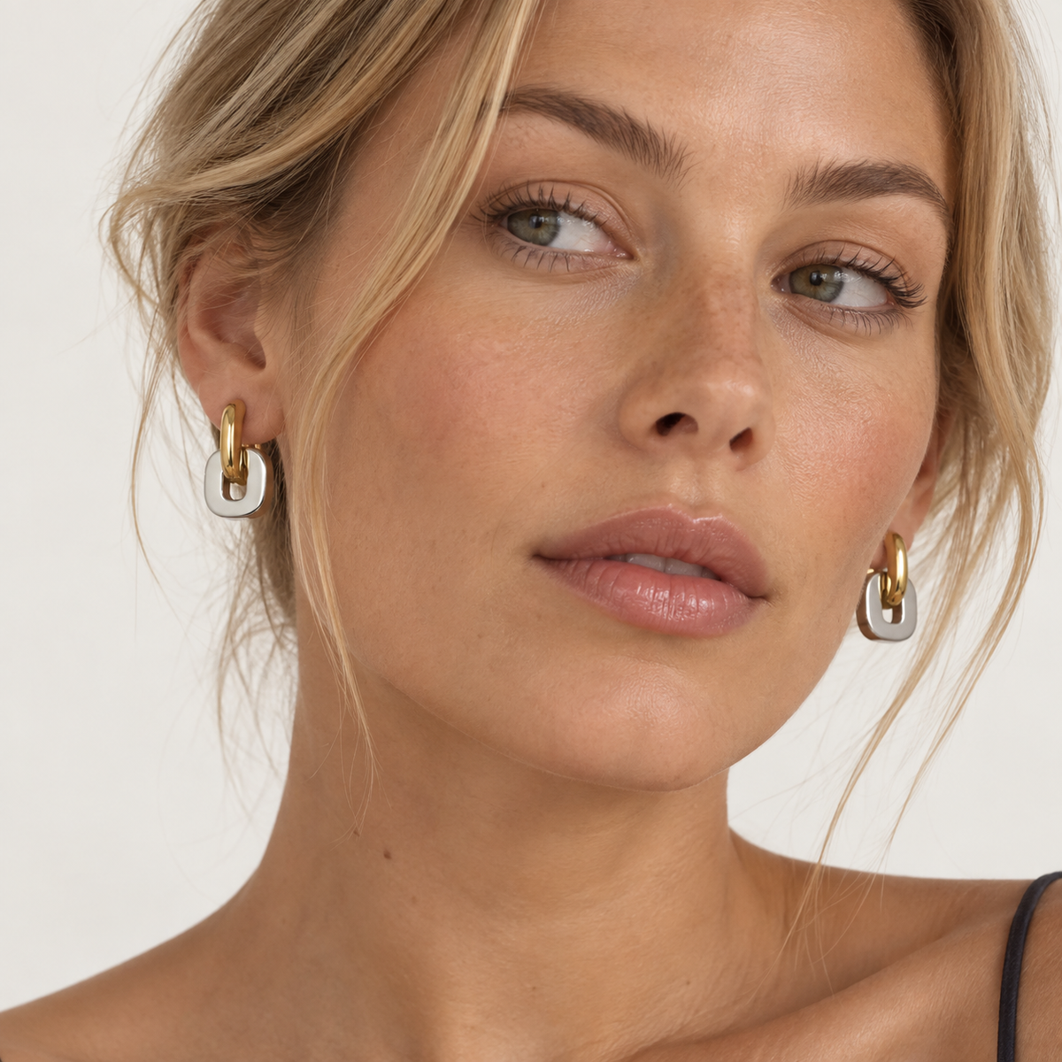 Close-up of a woman wearing gold and silver link hoop earrings against a clean white background.