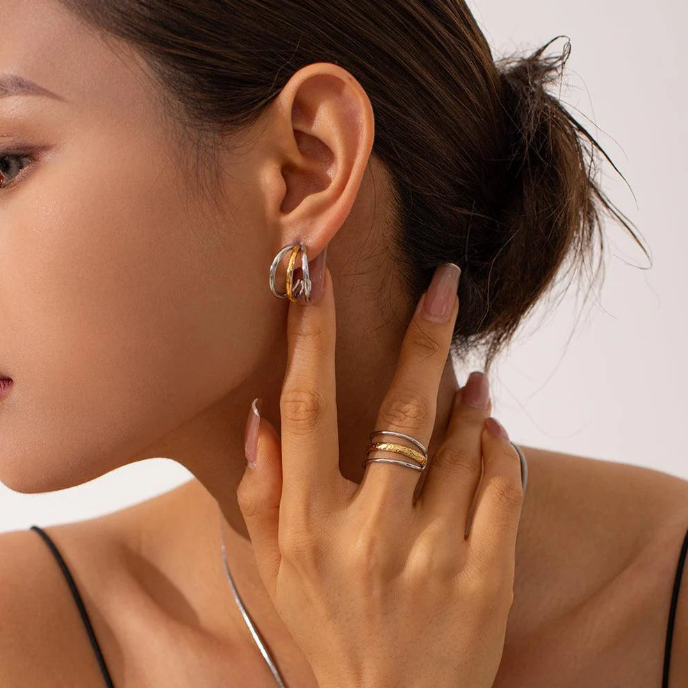 Close-up of a woman wearing gold hoop earrings and rings on a plain background