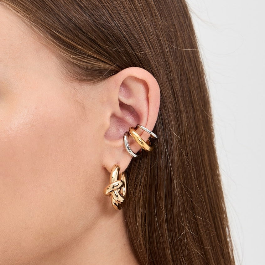 Close-up of a person wearing gold hoop earrings with a plain background