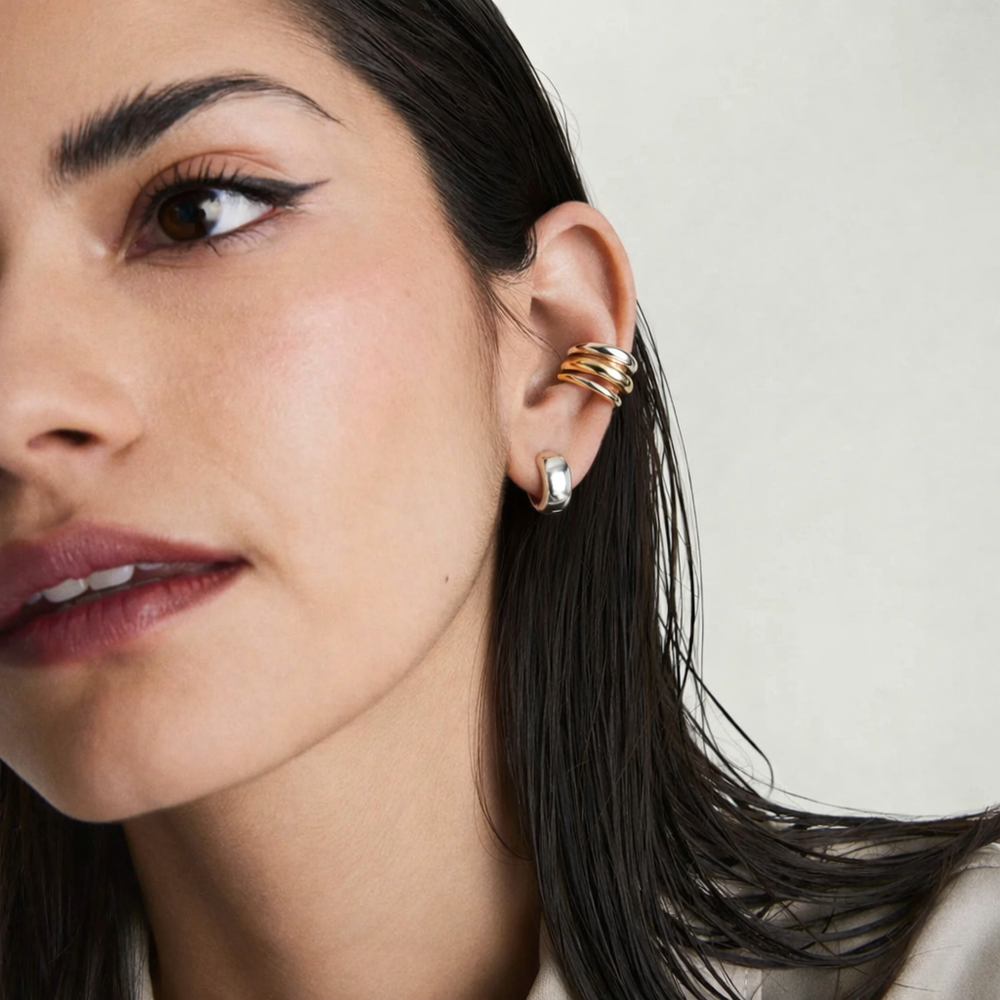 Close-up of a woman's ear with gold earrings against a neutral background