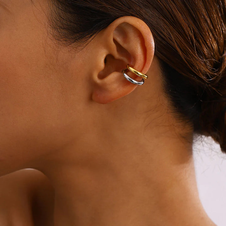 Close-up of an ear wearing two gold hoop ear cuff with a blurred background