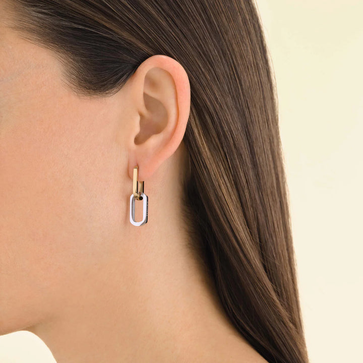 Close-up of a person wearing a gold and silver hoop earring on a beige background