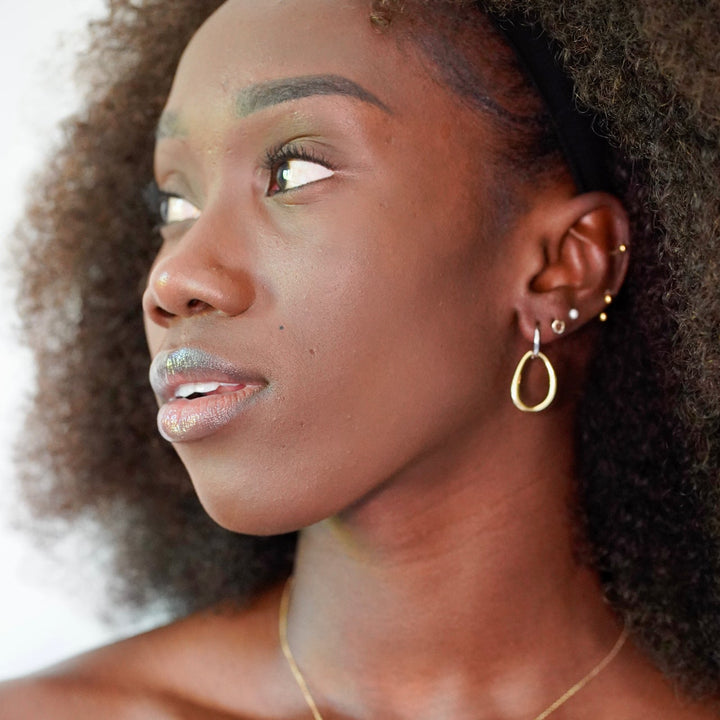 Woman wearing gold jewelry including earrings and a necklace, with a blurred background