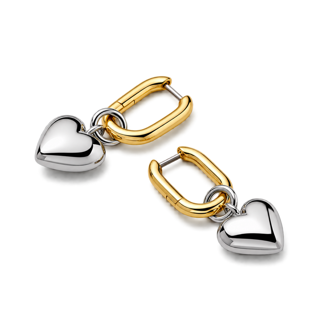 A pair of gold and silver drop earrings, each featuring a polished silver heart charm suspended from a gold huggie clasp, shown on a clean white background.