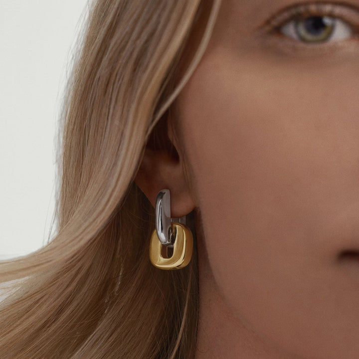 Close-up of a person wearing a gold and silver hoop earring.