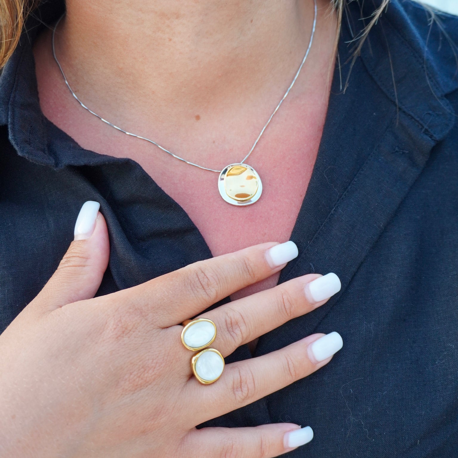 Close-up of a person wearing a necklace and two rings on a dark shirt.