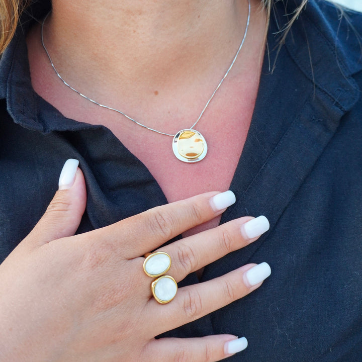 Close-up of a person wearing a necklace and two rings on a dark shirt.