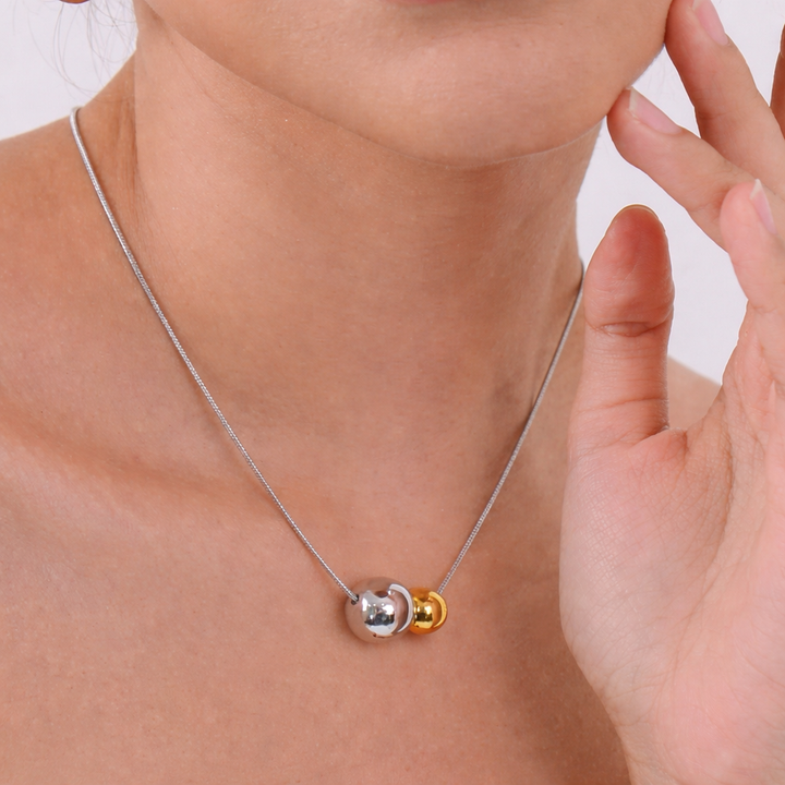 Necklace with two colored pendants being worn and adjusted by a hand.