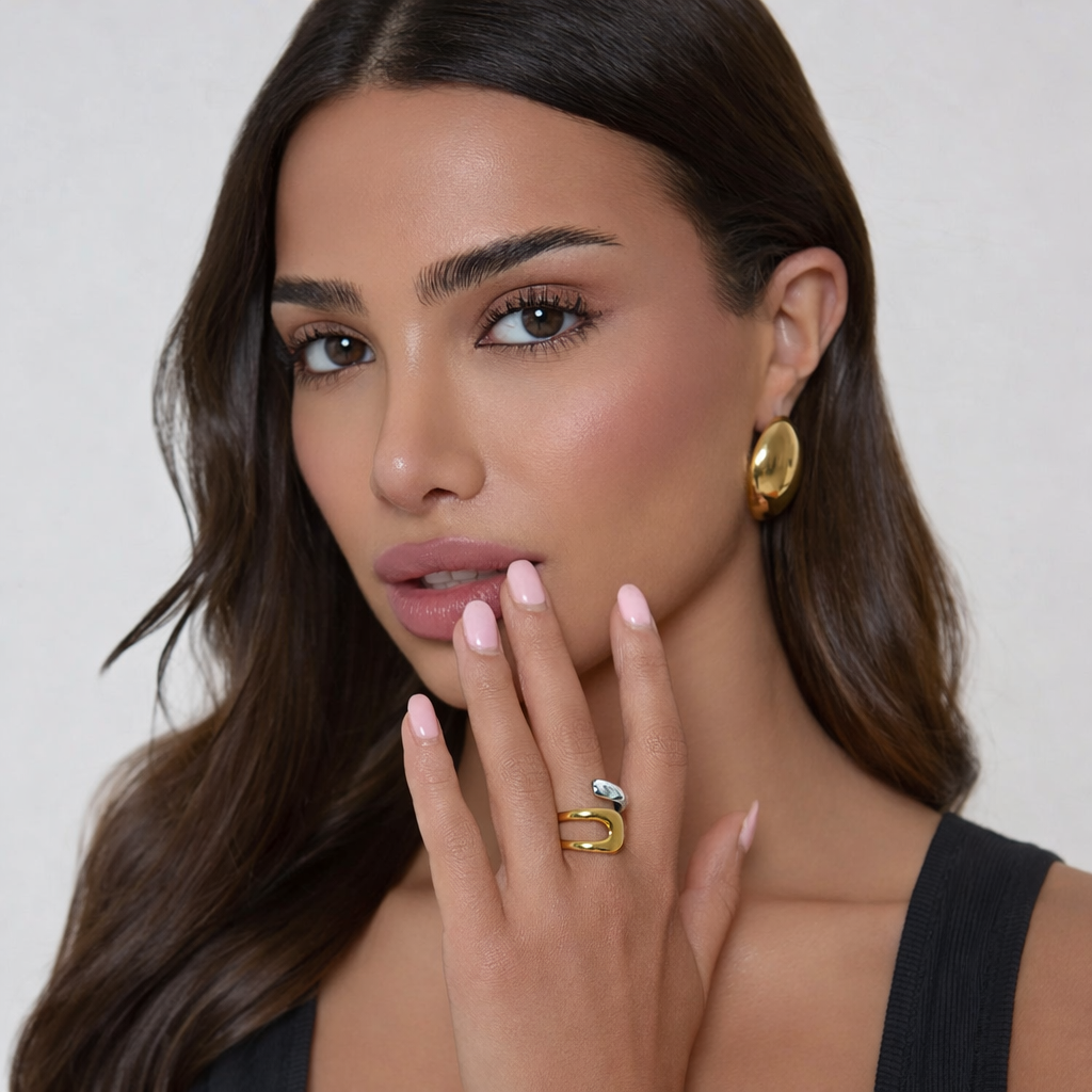 Woman wearing gold earrings and ring with a neutral background