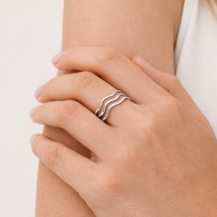Hand wearing a silver ring with wavy design on a neutral background