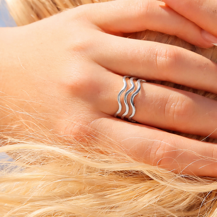 Hand wearing two silver wave-shaped rings on a blurred background of blonde hair