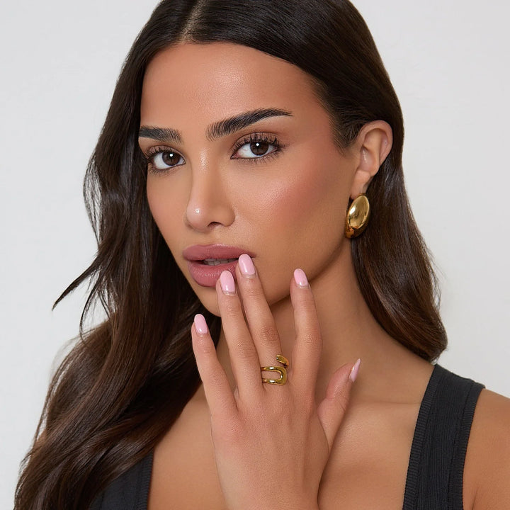 Woman wearing gold earrings and ring with a neutral background