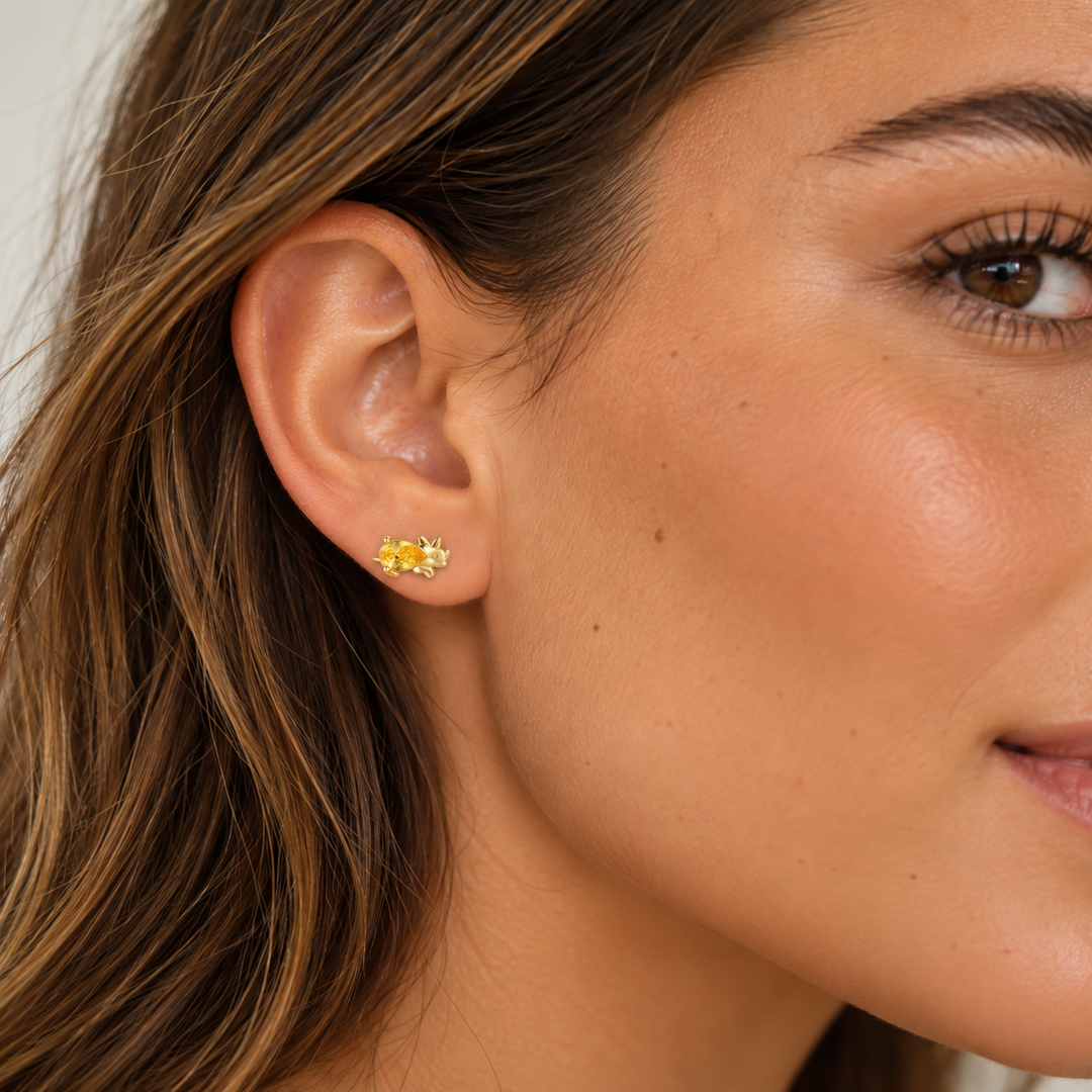 A close-up of a woman's ear wearing a small yellow stud earring with a textured gold setting.