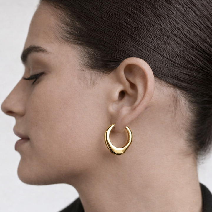 Close-up of a person wearing a gold hoop earring against a neutral background